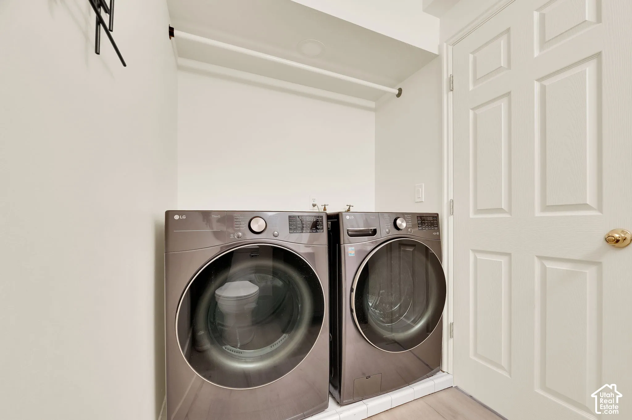 Dedicated laundry area featuring front-loading appliances, overhead shelving, and light wood-finish flooring