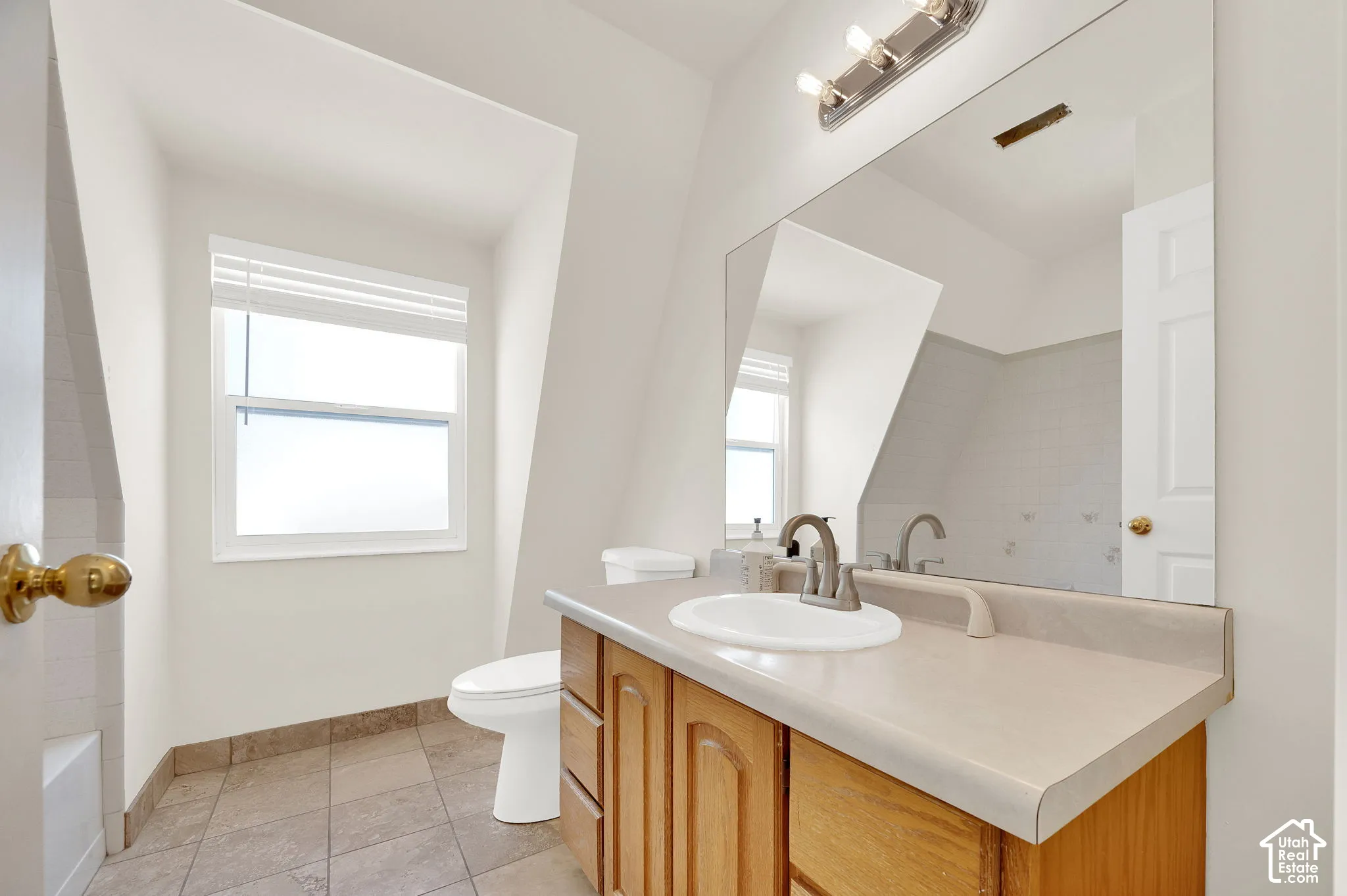 Bathroom featuring a single window with blinds, a toilet, and a vanity with a countertop sink