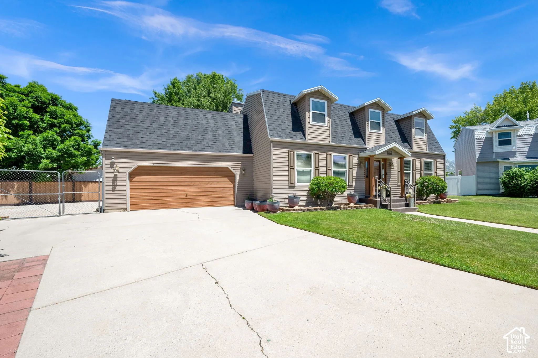 Gambrel-style home featuring dormer windows, a covered entry, and an attached garage with a wood-finish door