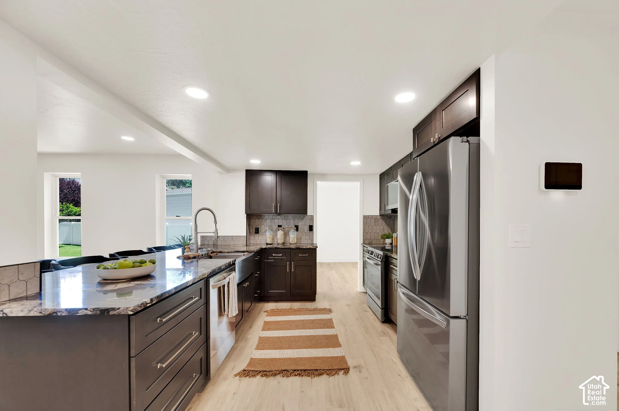 Spacious kitchen featuring dark wood cabinetry, granite countertops, stainless steel appliances, recessed lighting, and light wood-finish flooring