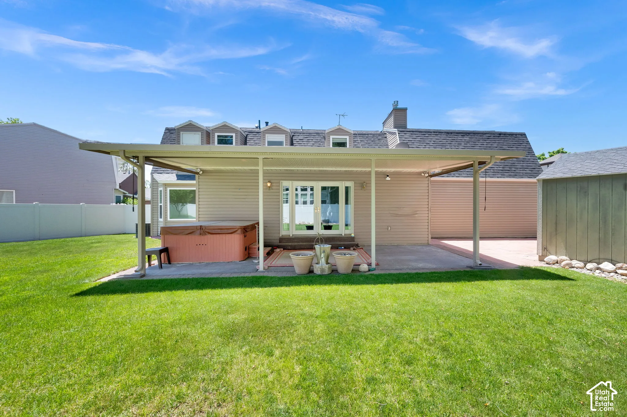 Expansive green lawn with a covered patio, featuring a hot tub, concrete and paver surfaces, and direct access to the interior via double glass doors