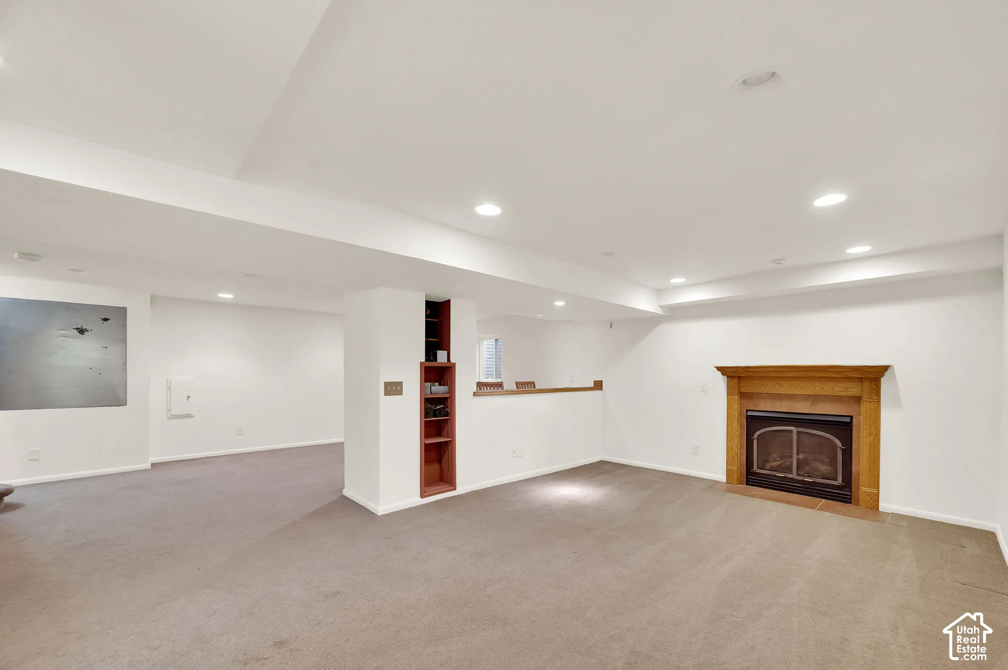 Spacious room with a wood-mantled fireplace, recessed lighting, built-in shelving, and neutral carpeting