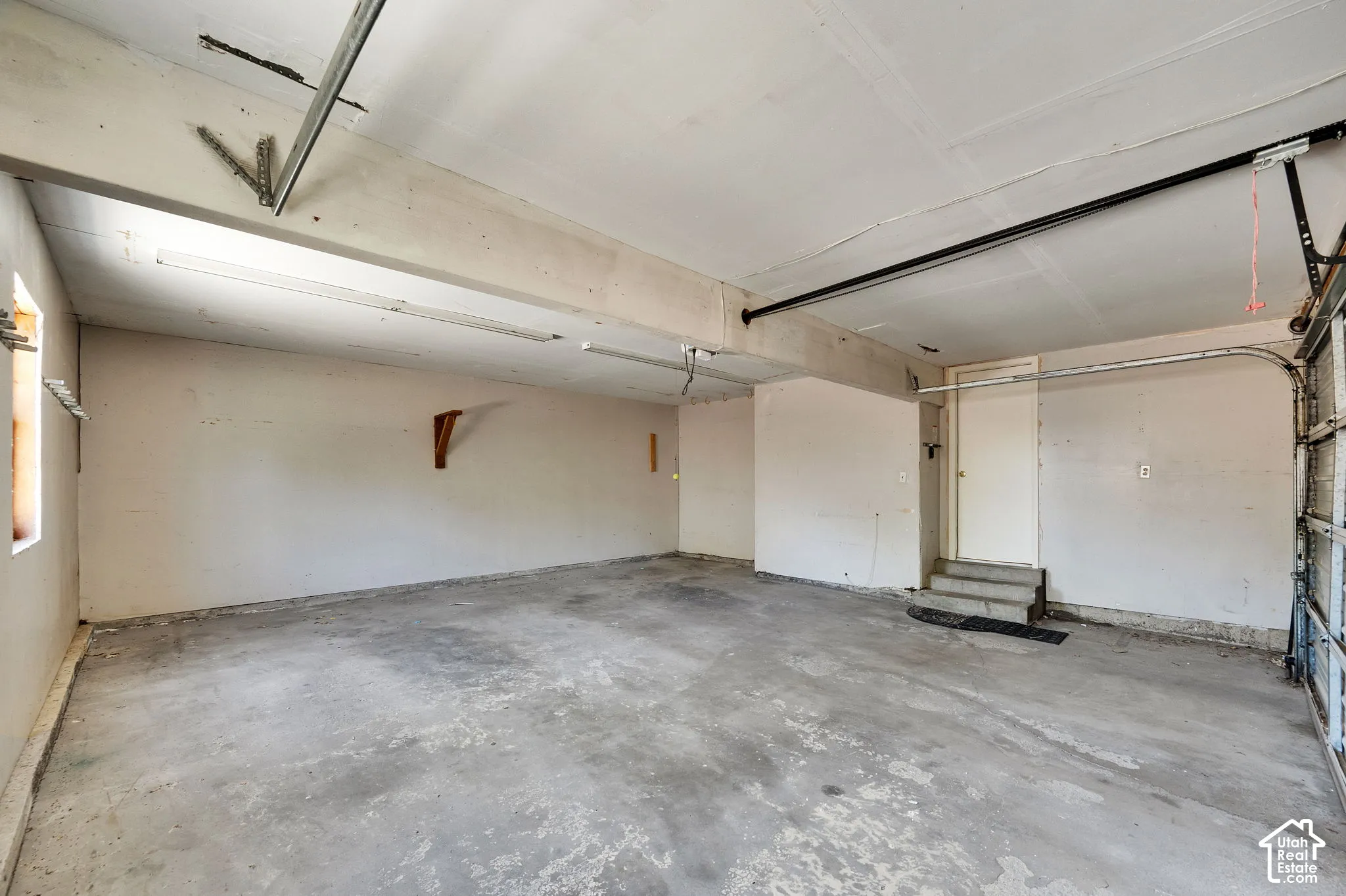 Spacious garage featuring concrete flooring, fluorescent overhead lighting, a service door, and an overhead garage door opening
