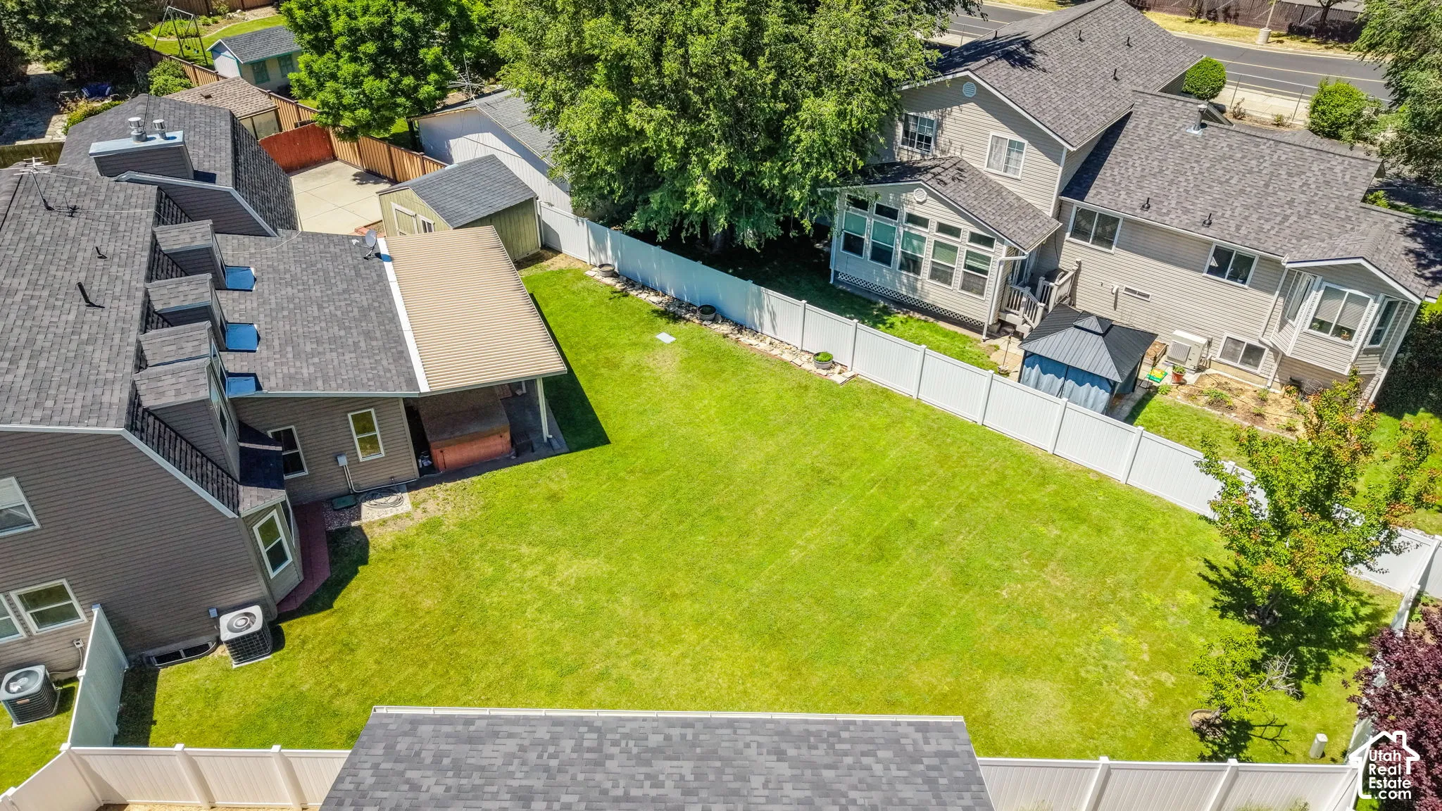 Expansive fenced backyard featuring a substantial lawn, covered patio, and a separate storage shed