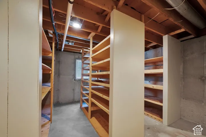 Spacious unfinished lower level featuring extensive built-in wooden shelving units, exposed ceiling joists, concrete walls, and concrete flooring
