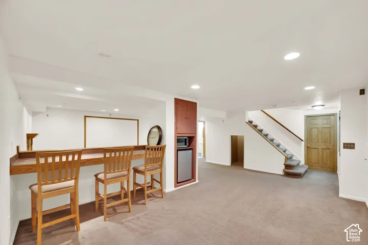 Finished lower level featuring a built-in bar with wood-finish countertop, recessed lighting, carpeted flooring, a built-in microwave, and a compact refrigerator
