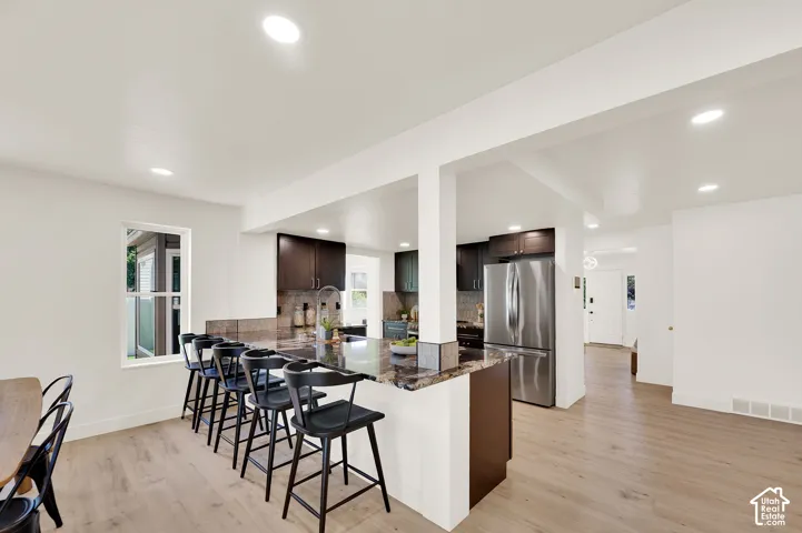 Kitchen featuring dark wood cabinetry, stainless steel refrigerator, and an island with a stone countertop and seating for five