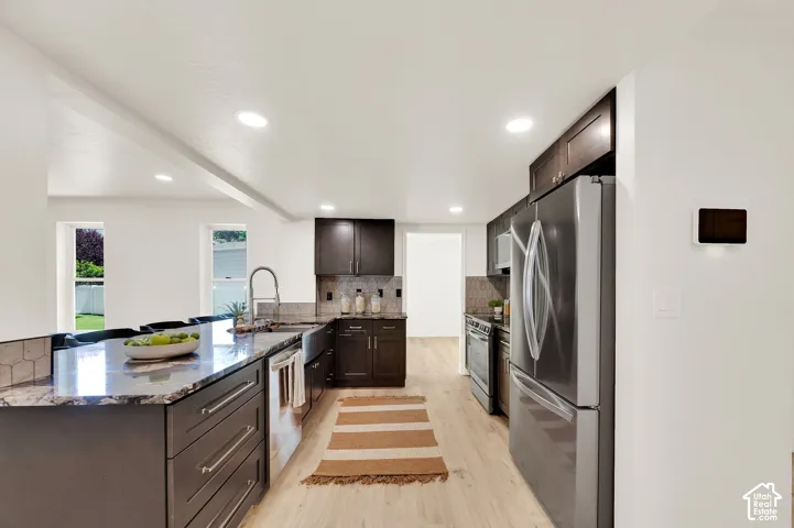 Spacious kitchen featuring dark wood cabinetry, granite countertops, stainless steel appliances, recessed lighting, and light wood-finish flooring