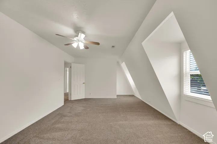 Spacious room featuring sloped ceilings, white walls, and neutral carpeting