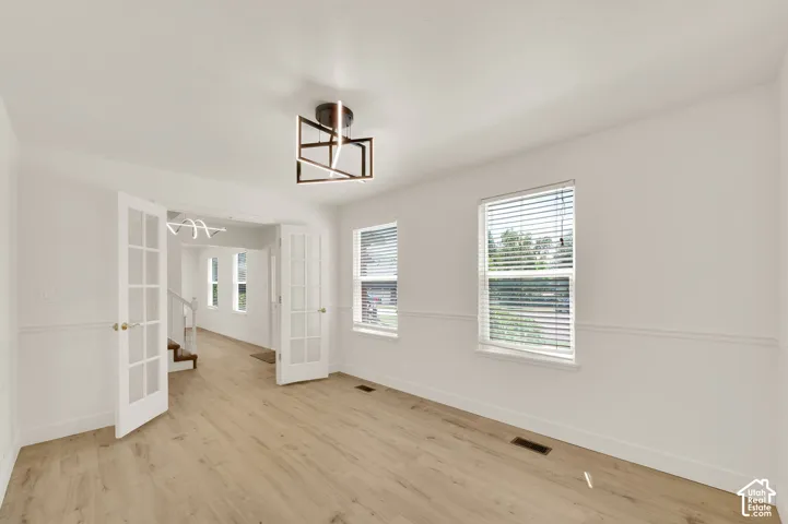 Room featuring light wood-finish flooring, white walls with wainscoting, and a modern geometric ceiling light fixture