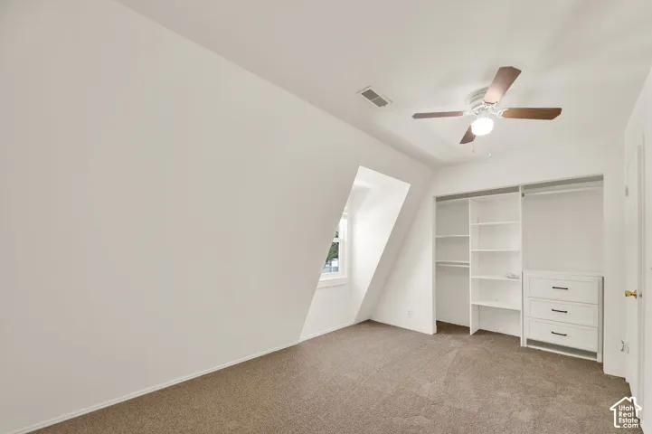 Attic room featuring a sloped ceiling, window, built-in shelving, built-in drawers with dark hardware, and a ceiling fan