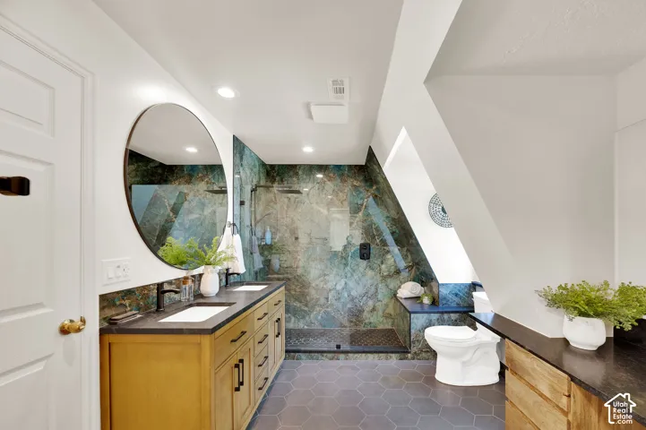 Spacious bathroom featuring a dual vanity with undermount sinks, hexagon tile flooring, a walk-in shower with glass enclosure, and accent stone tile work