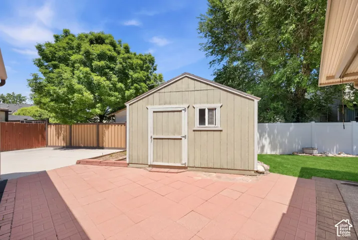 Detached storage shed featuring a small window and a solid door, positioned on a red brick paver patio