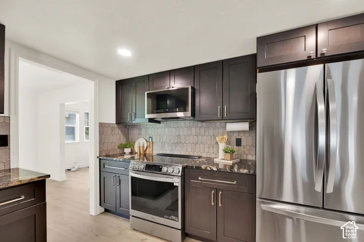 Kitchen featuring dark wood-finish cabinetry, stainless steel appliances, dark stone countertops, and a patterned tile backsplash