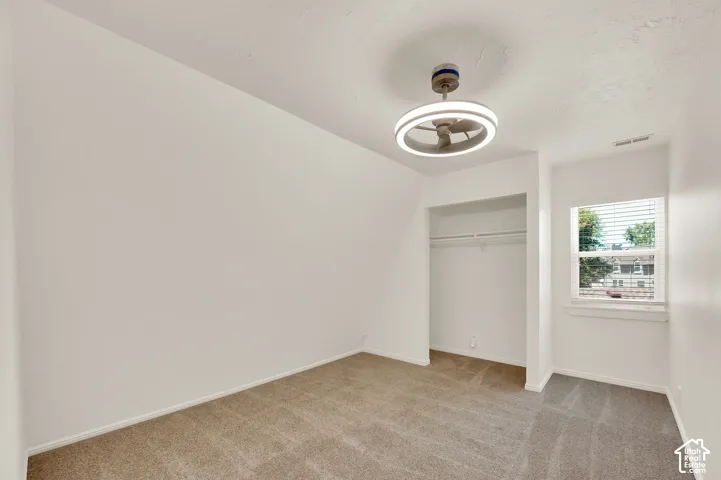 Carpeted room featuring a modern ceiling fan with integrated lighting, a window with horizontal blinds, and a built-in closet with shelving