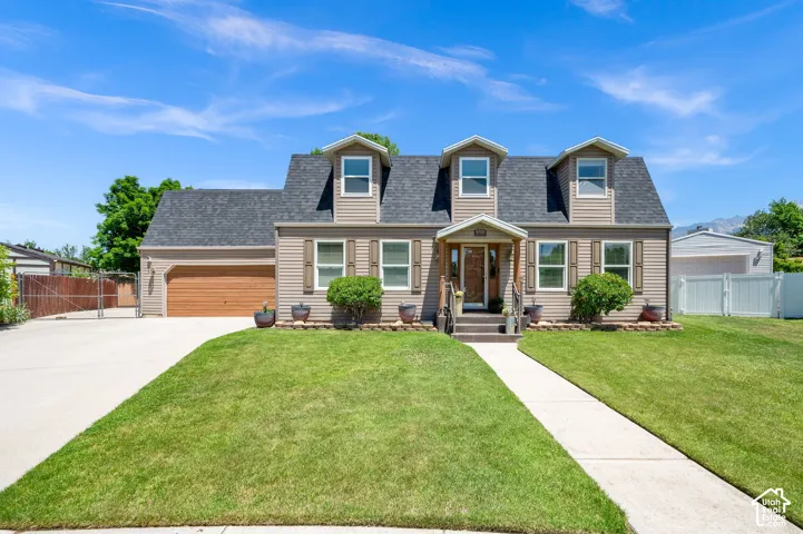 Traditional home with dormer windows, a covered entry porch, attached garage with wood-finish door, concrete driveway, and a concrete walkway