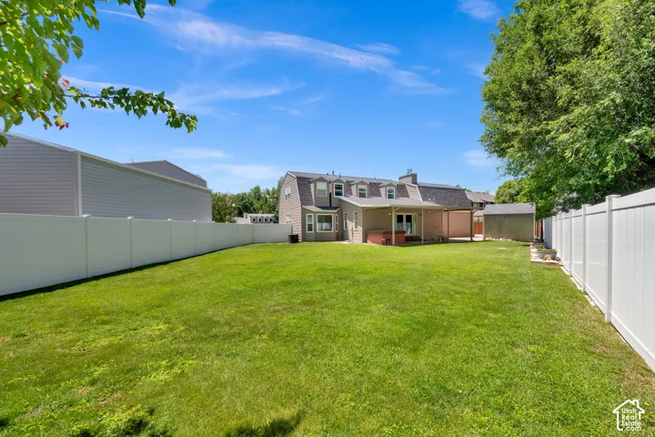Expansive fenced backyard featuring a manicured lawn, a covered patio, a storage shed, and mature trees