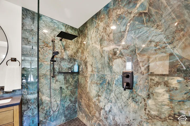 Walk-in shower featuring full-height natural stone-finish walls, a glass enclosure, matte black fixtures, a built-in shower niche, and hexagonal tile flooring