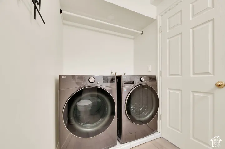 Dedicated laundry area featuring front-loading appliances, overhead shelving, and light wood-finish flooring