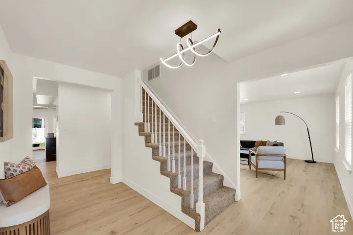 Entry foyer featuring light wood-finish flooring, a contemporary spiral chandelier, and a carpeted staircase with white railings