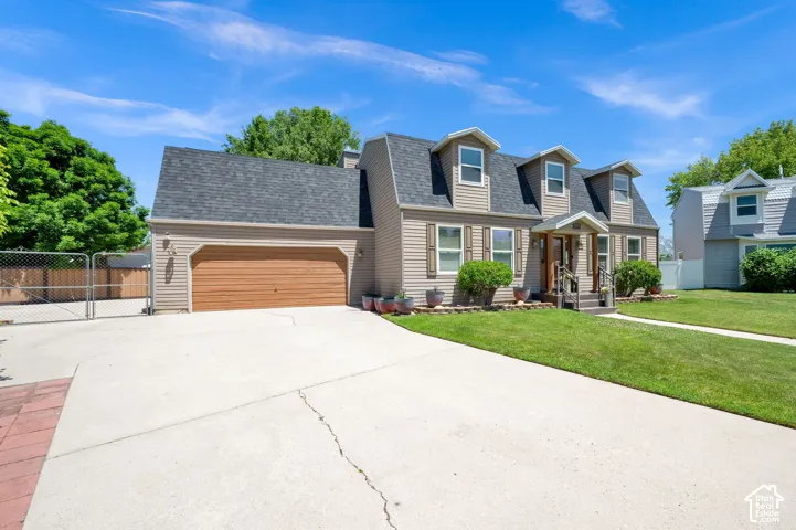 Gambrel-style home featuring dormer windows, a covered entry, and an attached garage with a wood-finish door