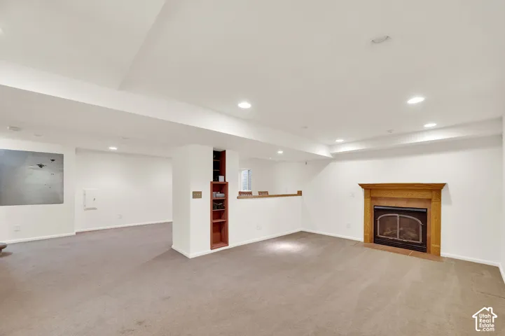 Spacious room with a wood-mantled fireplace, recessed lighting, built-in shelving, and neutral carpeting