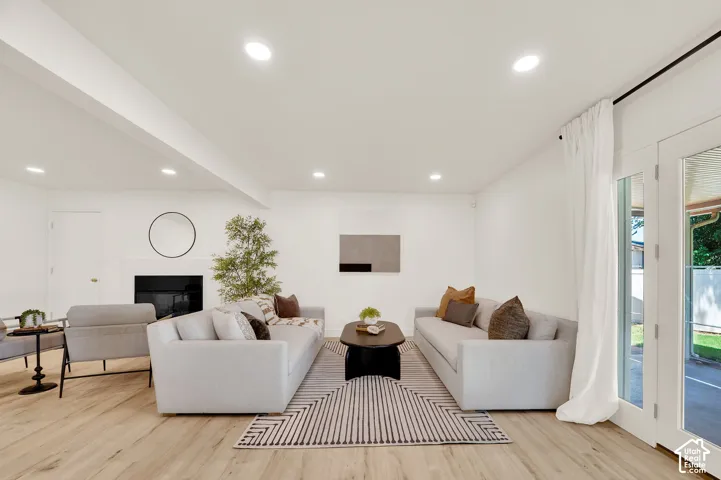 Spacious living area featuring light wood-finish flooring, recessed lighting, and a white-painted fireplace