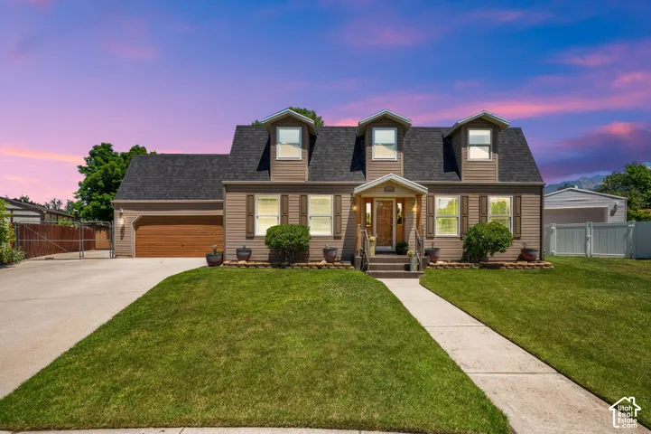 Dormer-style home featuring tan horizontal siding, a dark shingle roof, and a wood-finish garage door