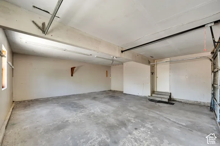 Spacious garage featuring concrete flooring, fluorescent overhead lighting, a service door, and an overhead garage door opening
