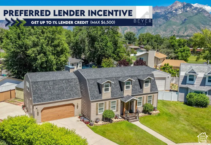 Gambrel-style exterior featuring neutral vinyl siding, an attached two-car garage, three prominent roof dormers, a concrete driveway, and mountain scenery