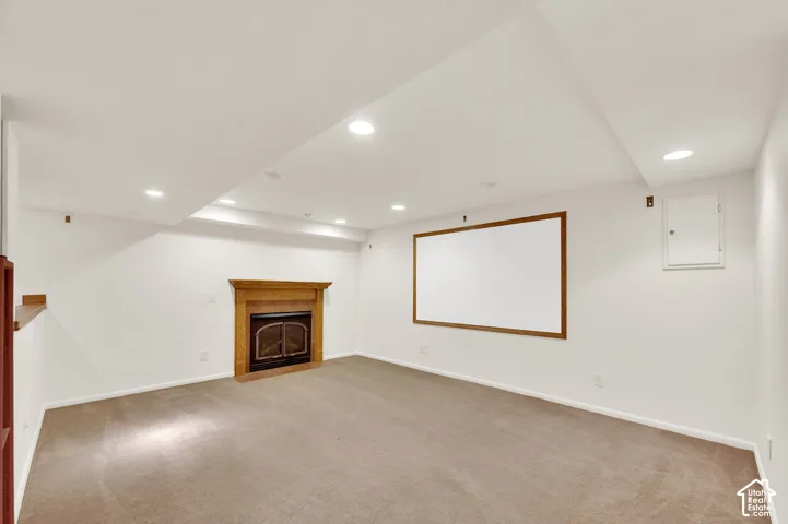 Recessed lighting illuminates this carpeted room featuring a wood-mantled fireplace with an iron grate