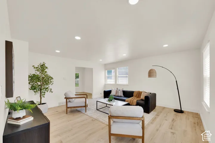 Bright living area featuring wood-finish flooring, recessed lighting, white walls, and multiple windows with blinds