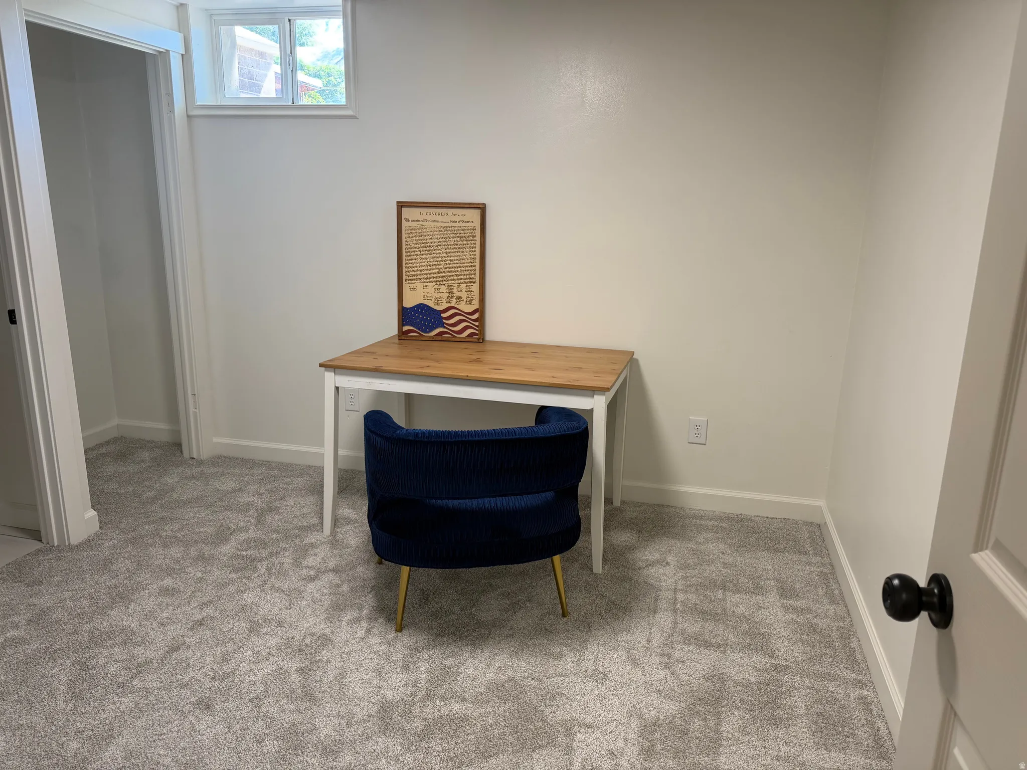 Brightly lit interior space featuring light gray carpeting, white walls, and a window providing natural illumination