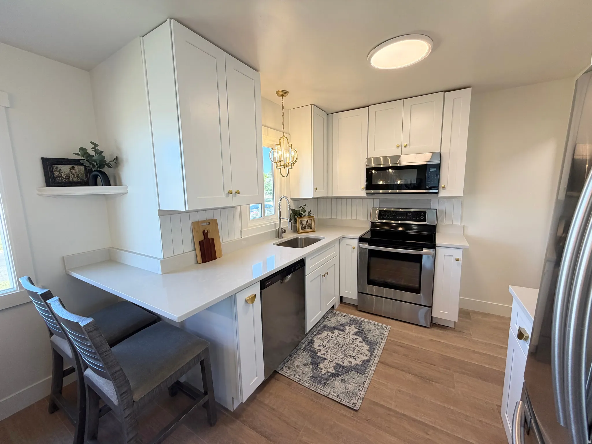 Well-appointed kitchen featuring white cabinetry, light-toned countertops, stainless steel appliances, and wood-finish flooring