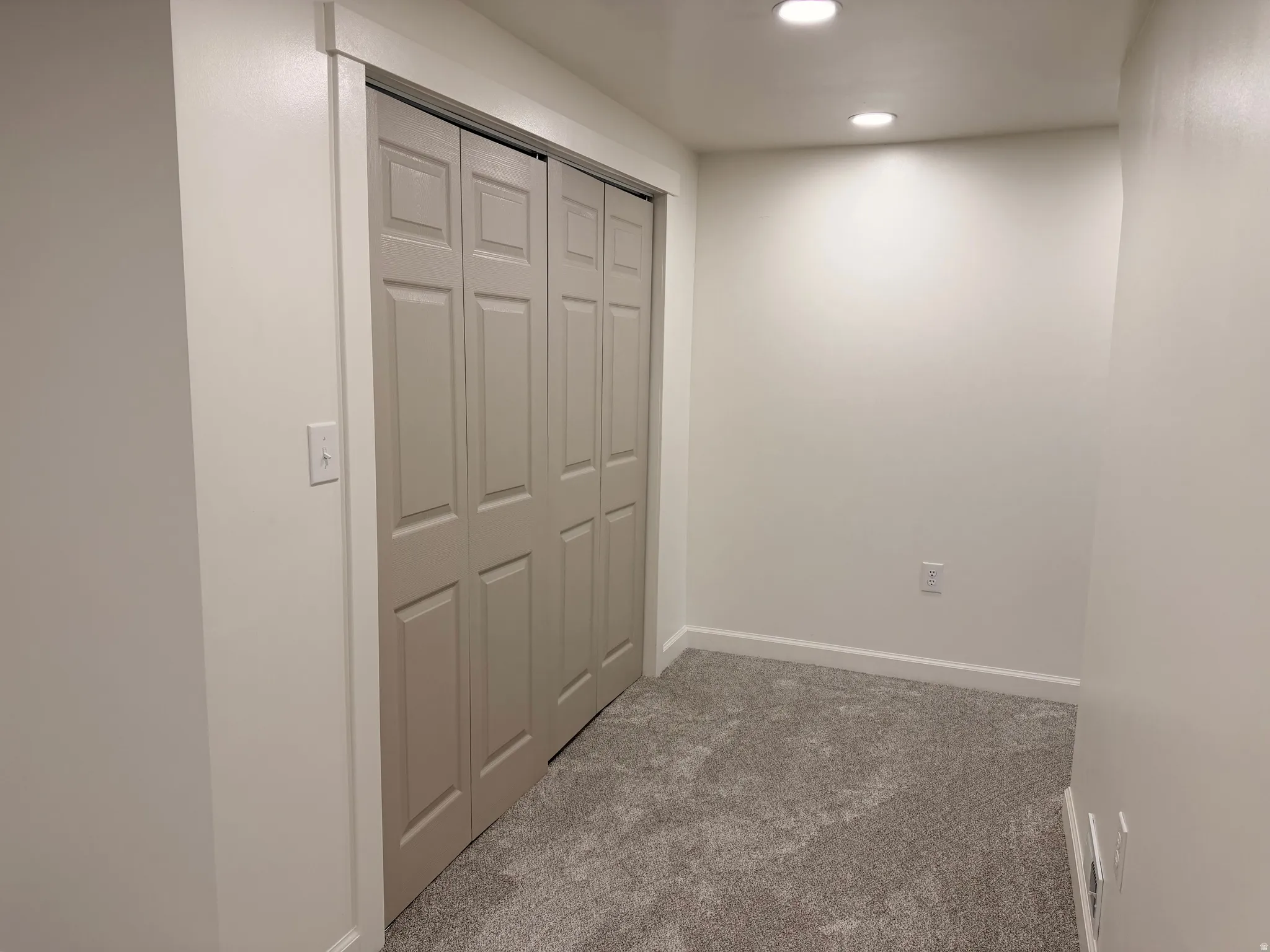 Built-in bi-fold closet doors, recessed lighting, neutral wall paint, white trim, and gray carpet