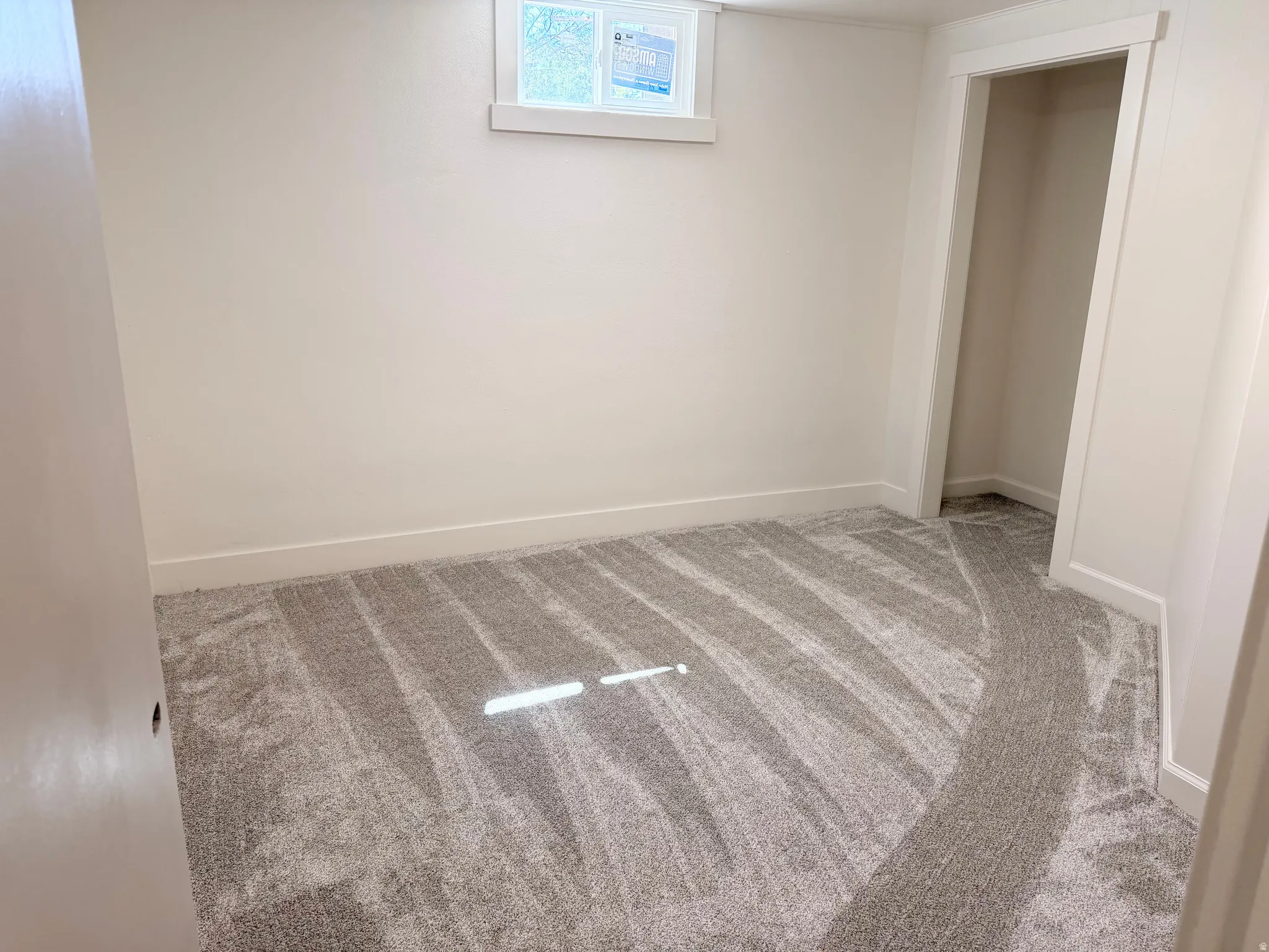 Neutral-toned room featuring a light gray carpet, white baseboards, and a single window with white trim