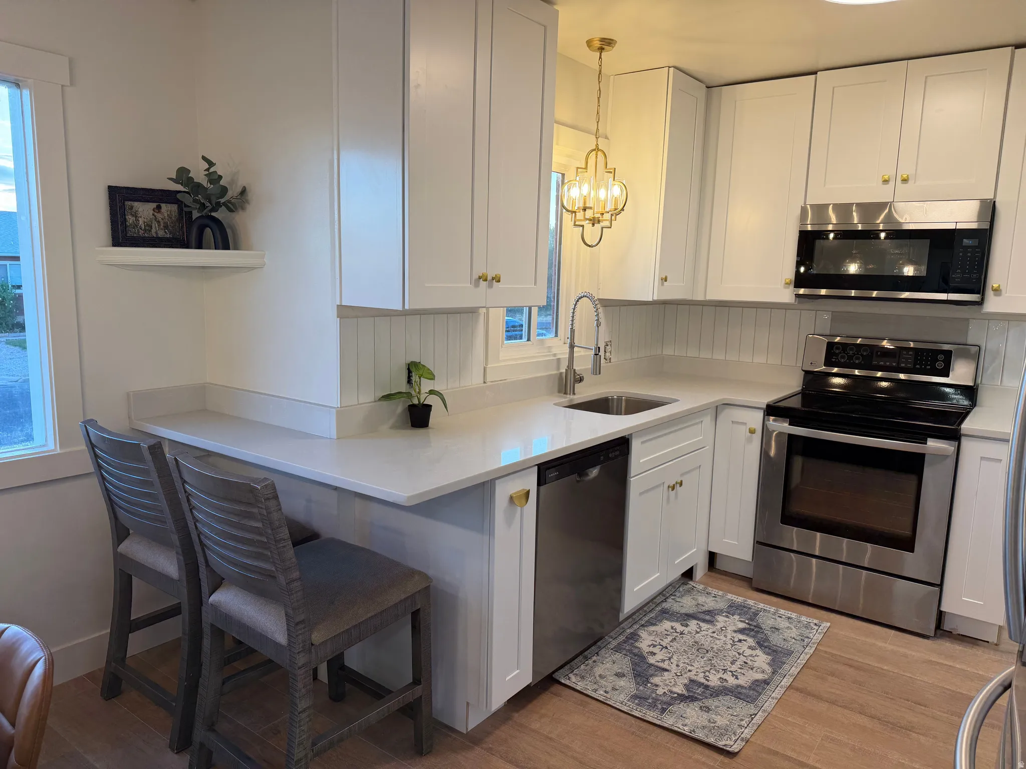 Modern kitchen featuring white shaker cabinetry, stainless steel appliances, light countertops, and wood-finish flooring