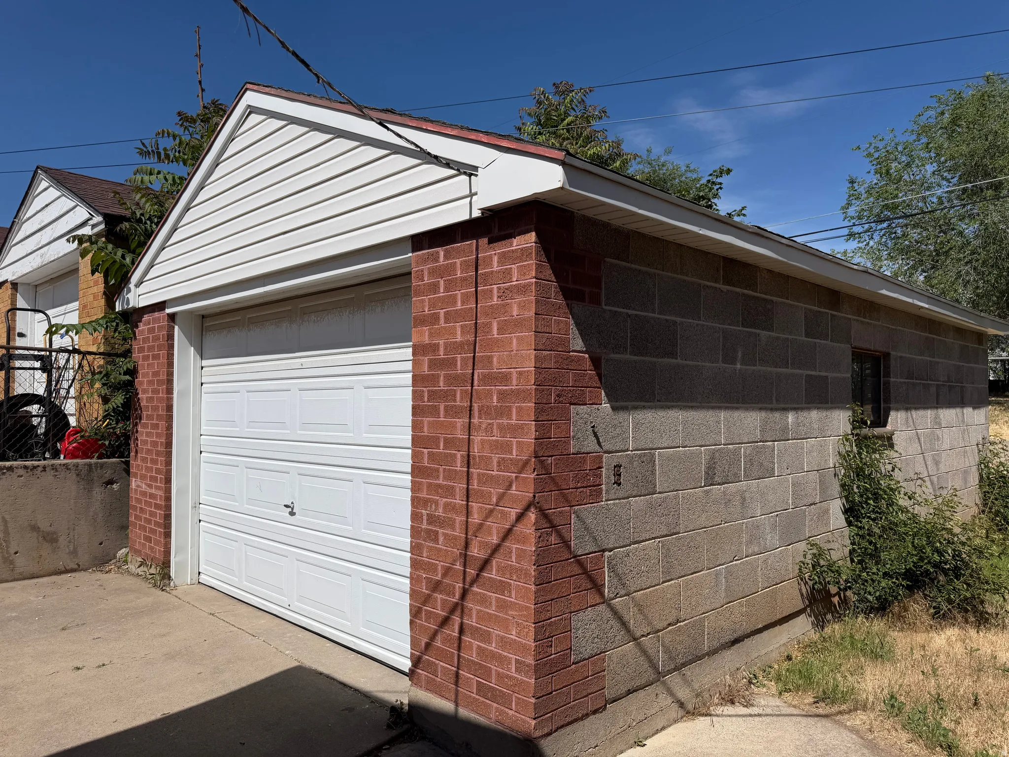 Detached garage featuring a white panel door, red brick facade, white vinyl siding on the gable, and concrete block construction