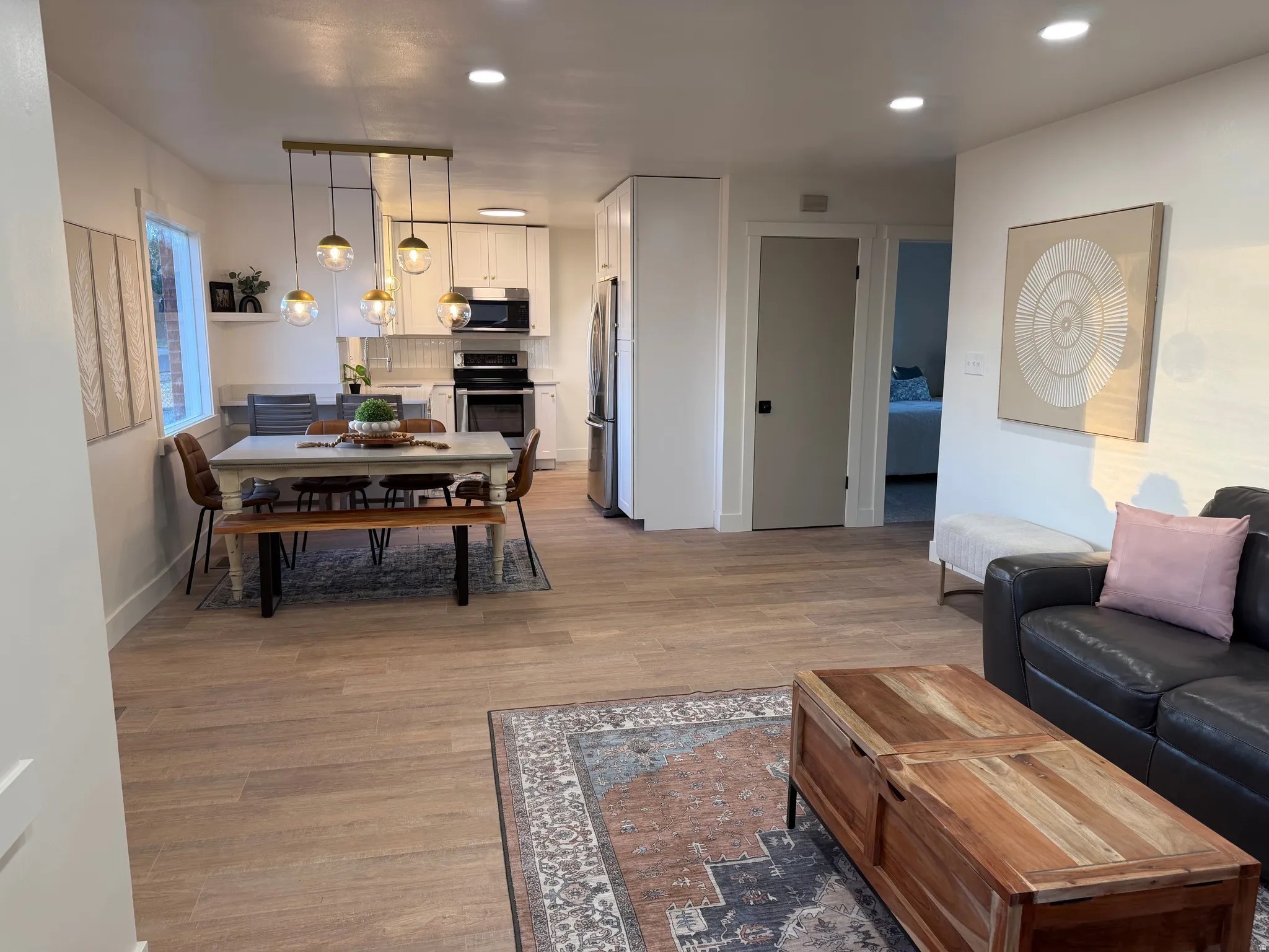 Open-concept living space featuring wood-finish flooring, recessed lighting, and a modern kitchen with white cabinetry and stainless steel appliances