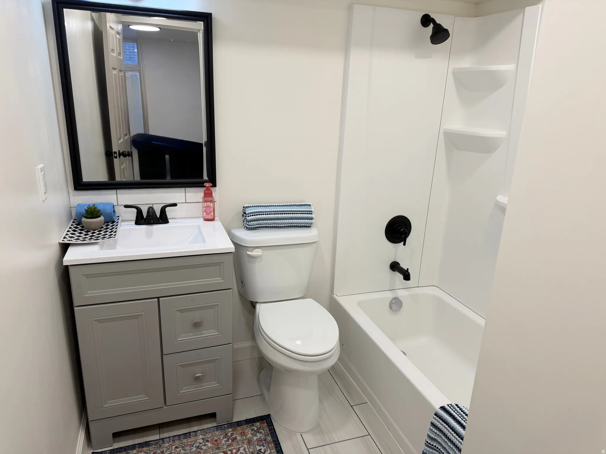 Bathroom featuring a white bathtub with a black shower fixture, a white toilet, and a vanity with a white countertop and gray cabinetry