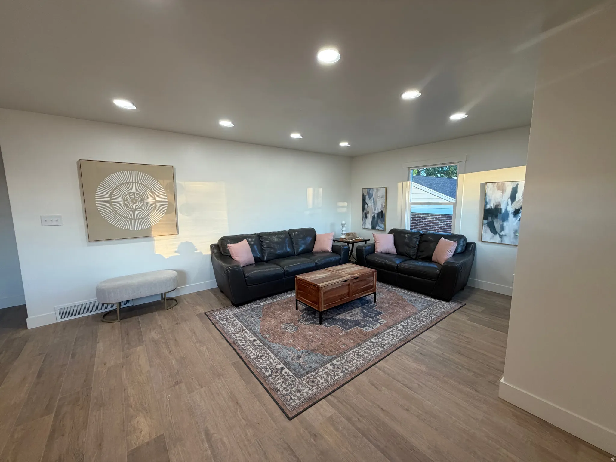 Spacious living area featuring light wood-finish flooring, recessed ceiling lighting, and crisp white walls