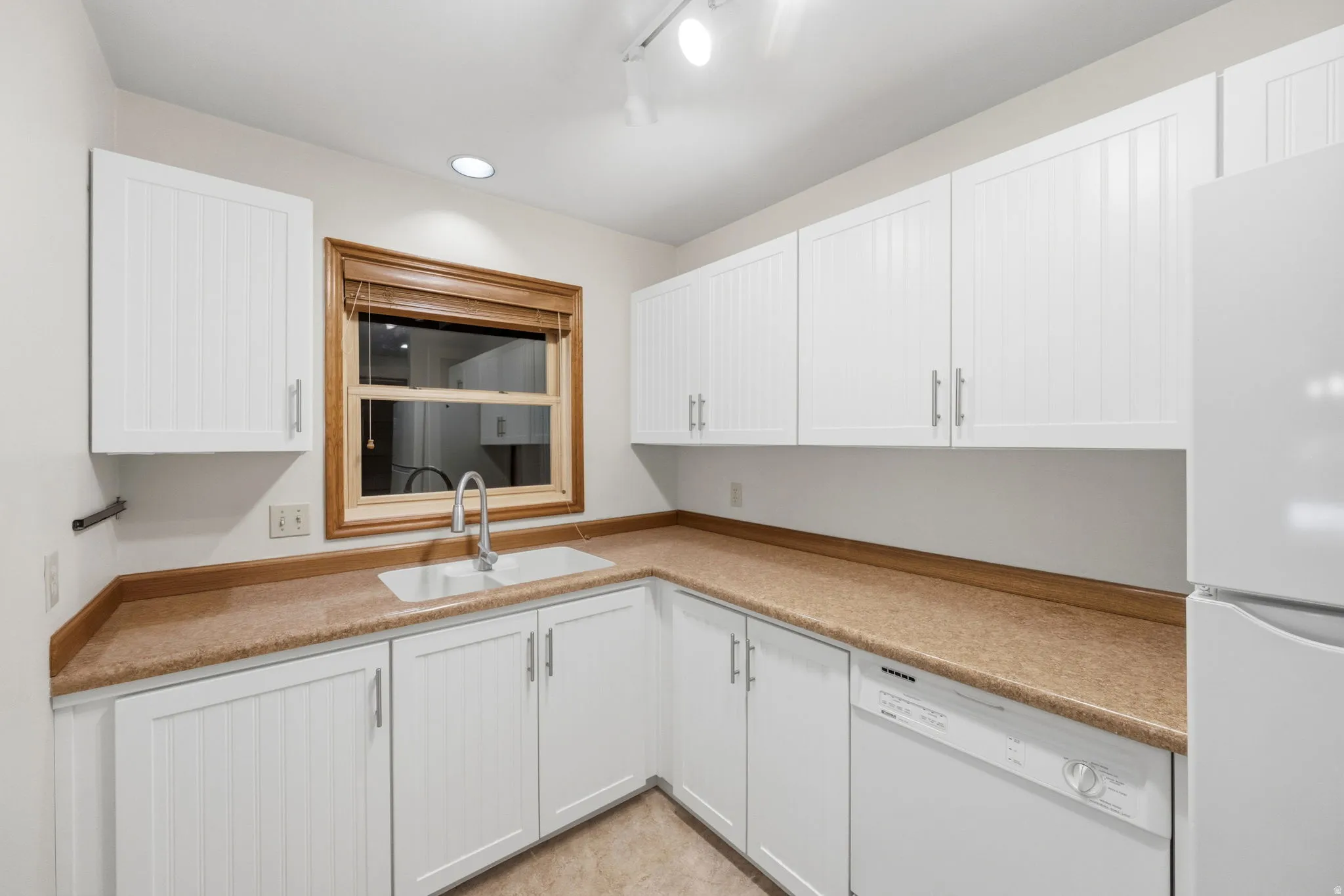 Kitchen featuring white cabinetry with brushed nickel hardware, a double basin sink with a gooseneck faucet, light brown countertops, and a white dishwasher