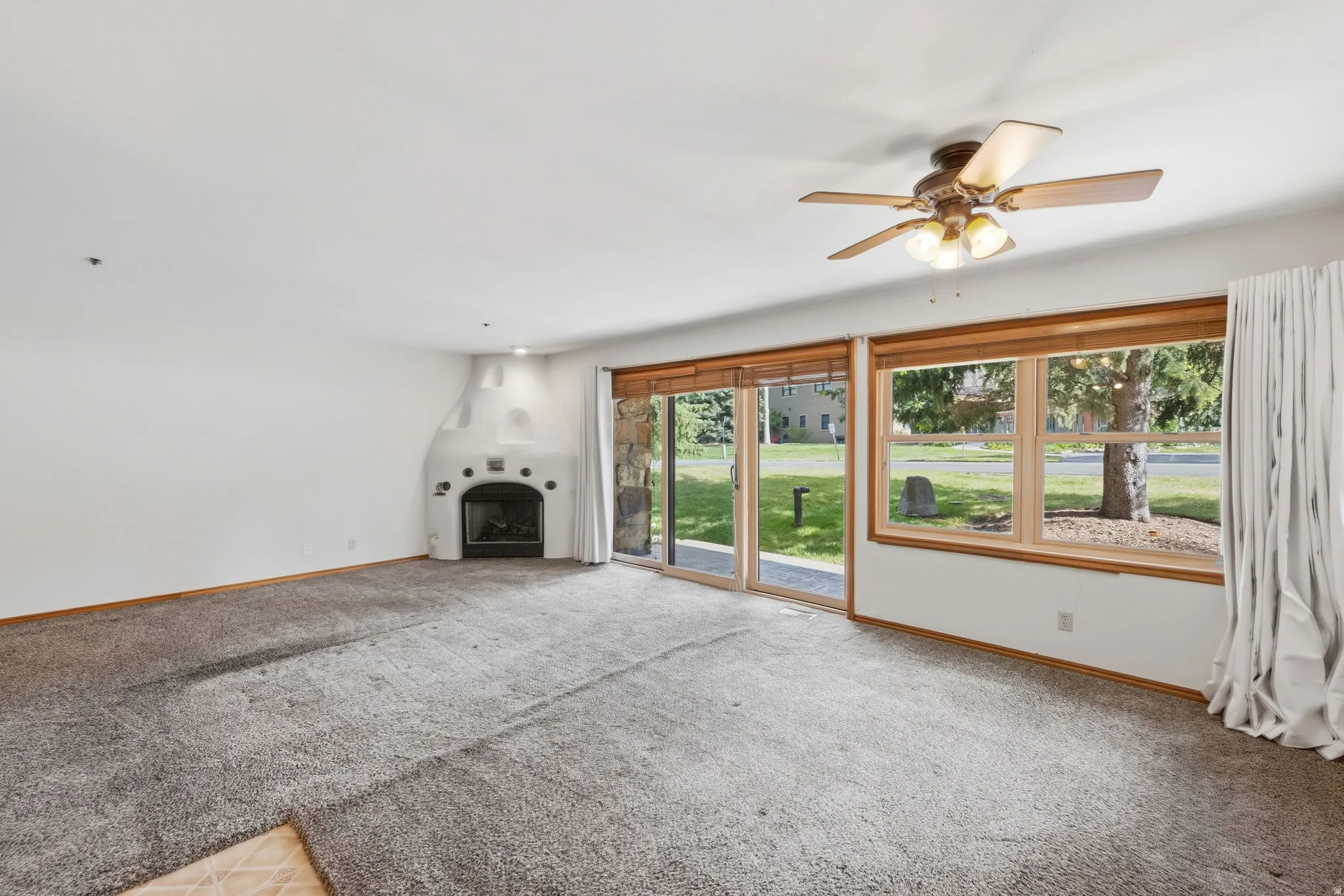 Living area featuring a southwestern-style fireplace, ceiling fan with integrated lighting, expansive windows with wood trim, and glass sliding doors
