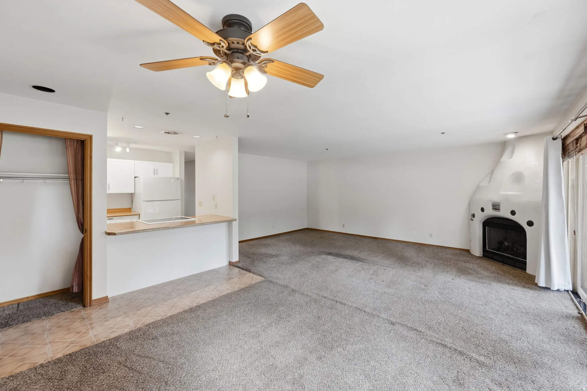 Living area featuring a textured carpet, a kiva-style fireplace, and a ceiling fan with integrated lighting
