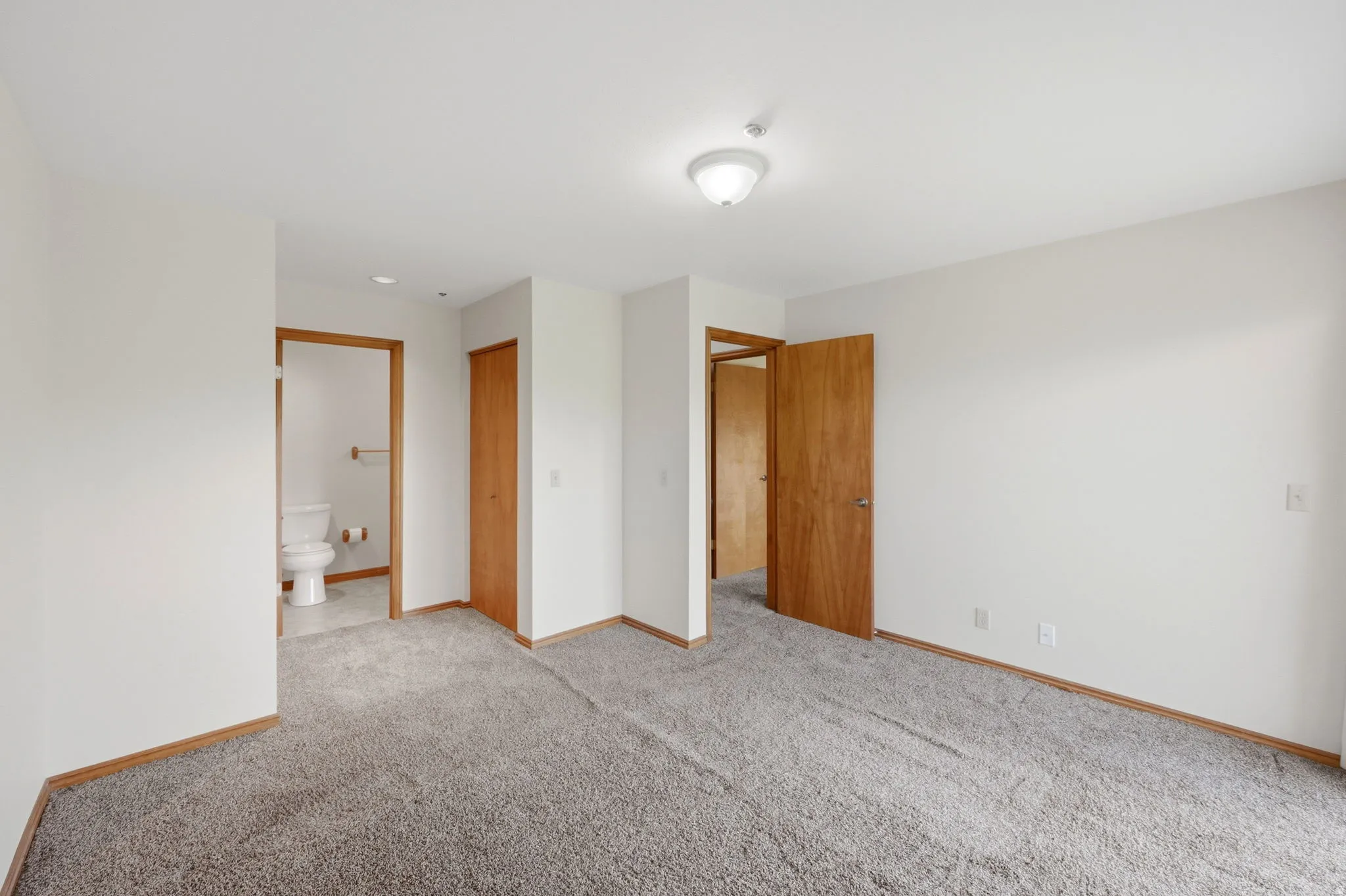 Spacious room featuring neutral carpeting, light-toned walls, wood-finish trim, and multiple doorways