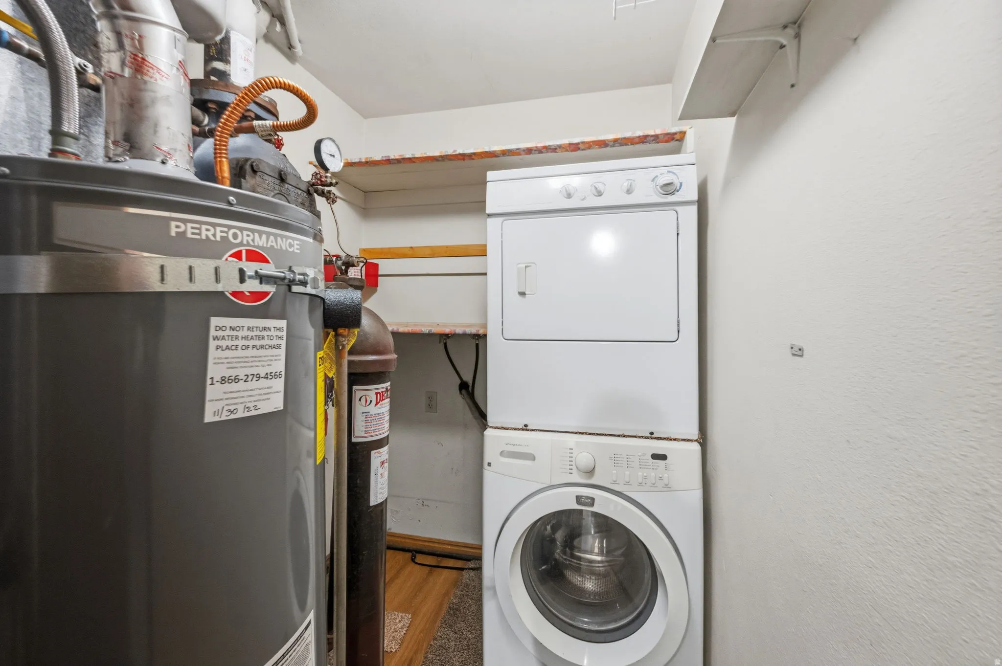 Utility area featuring a water heater, stacked washer and dryer, and wall-mounted shelving