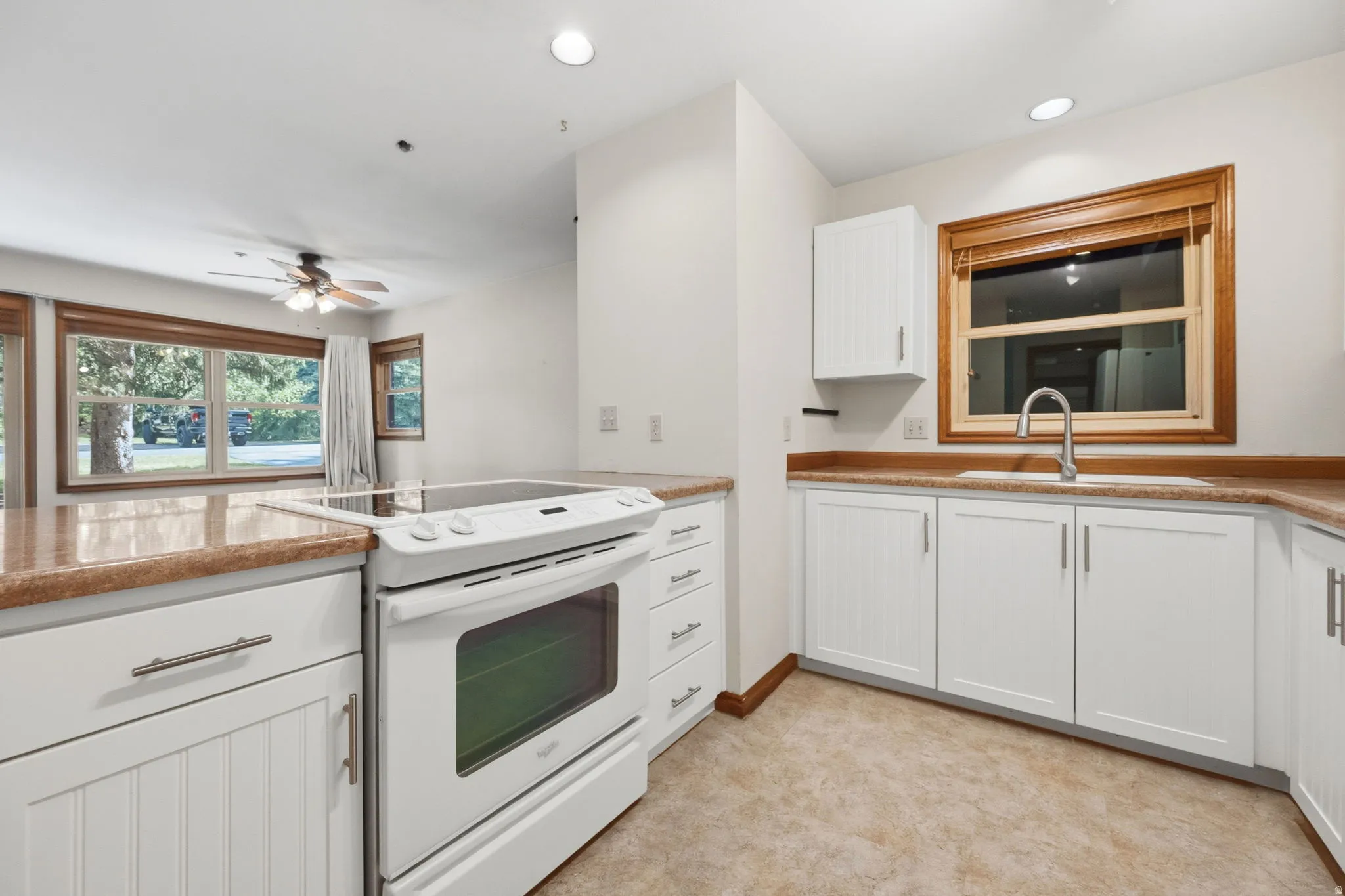 Kitchen featuring white cabinetry, light-toned countertops, a built-in electric range, a stainless steel sink with a gooseneck faucet, and tile flooring