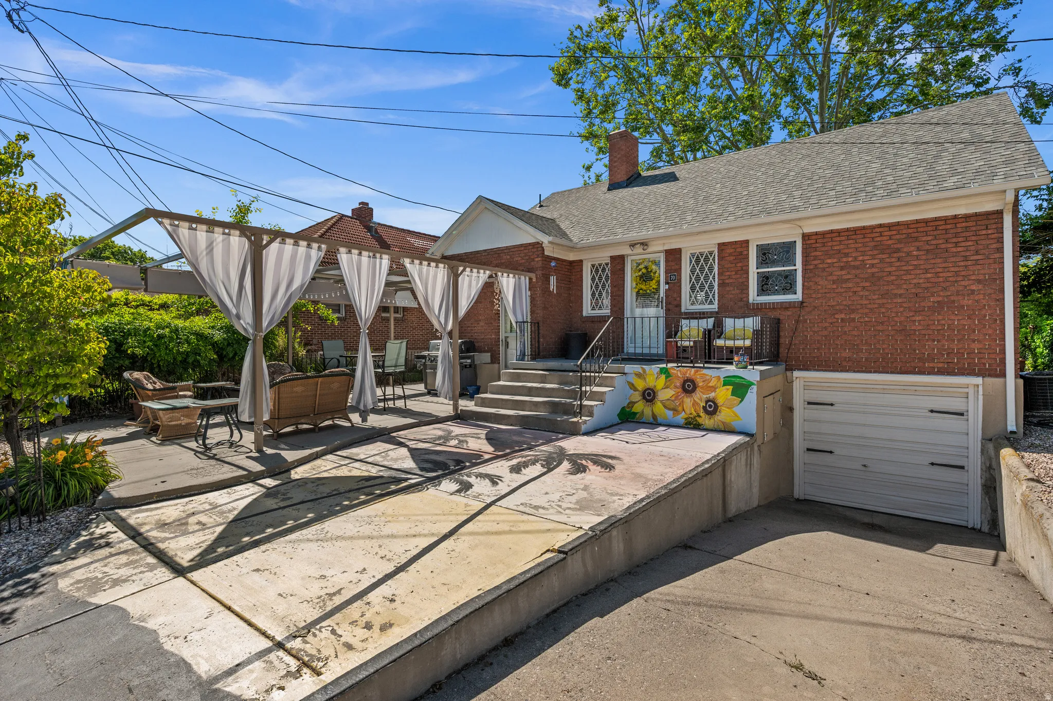 Red brick exterior featuring a multi-level concrete patio with a pergola, a built-in garage, a concrete driveway, and a painted retaining wall