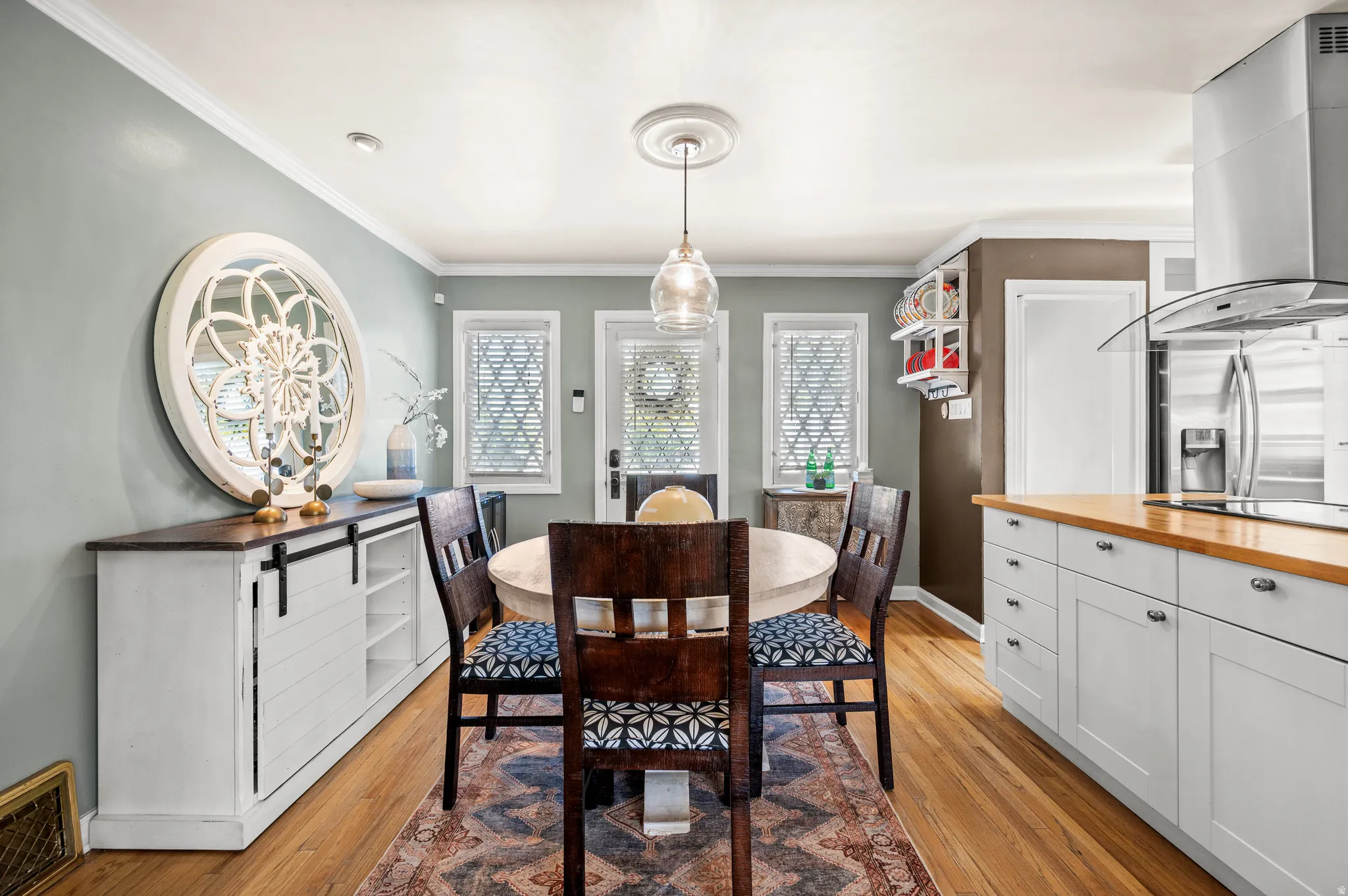 Dining area featuring wood-finish flooring, a contemporary pendant light fixture, and crown molding