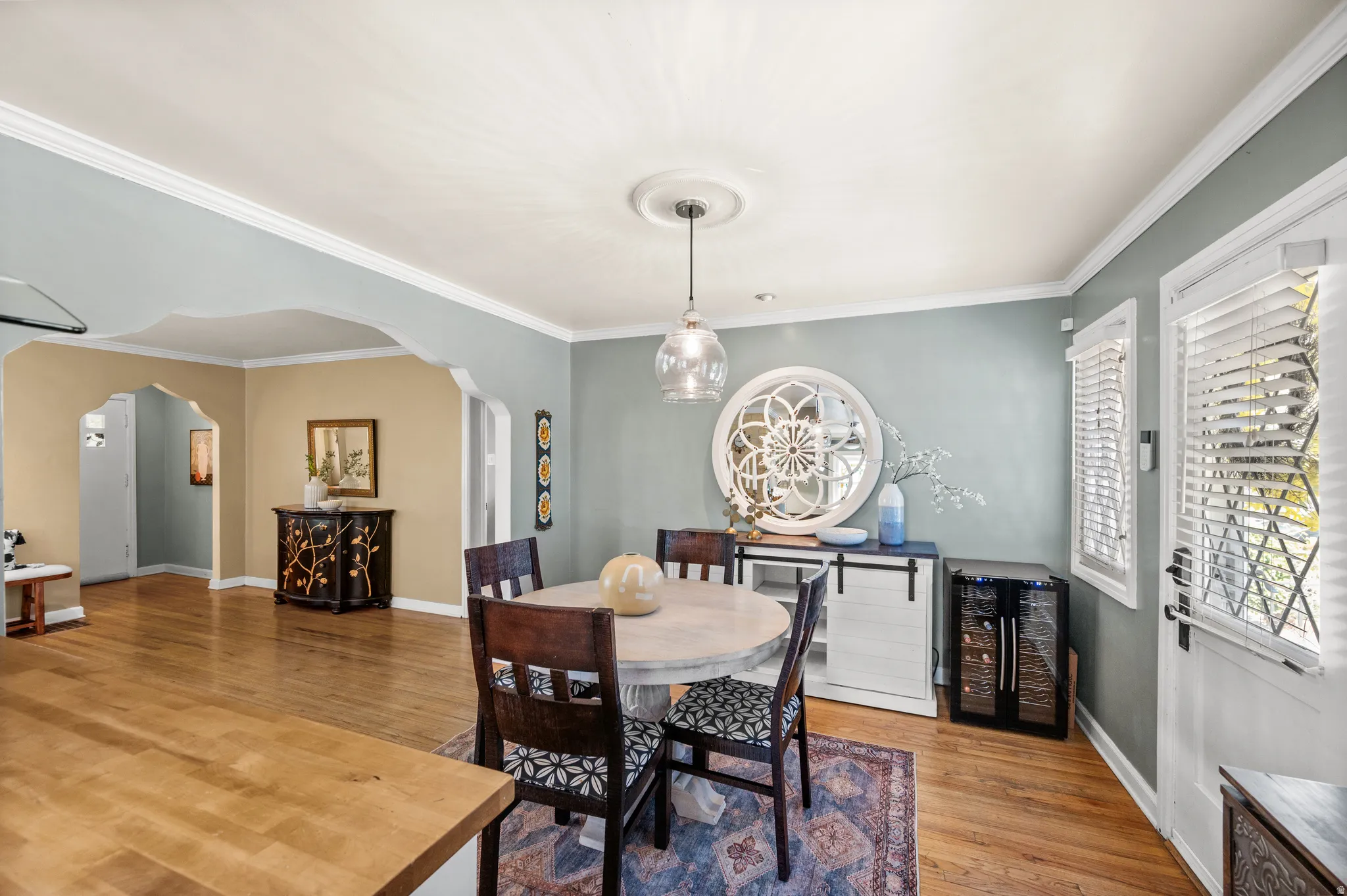 Dining area featuring wood-finish flooring, a contemporary pendant light fixture, and crown molding
